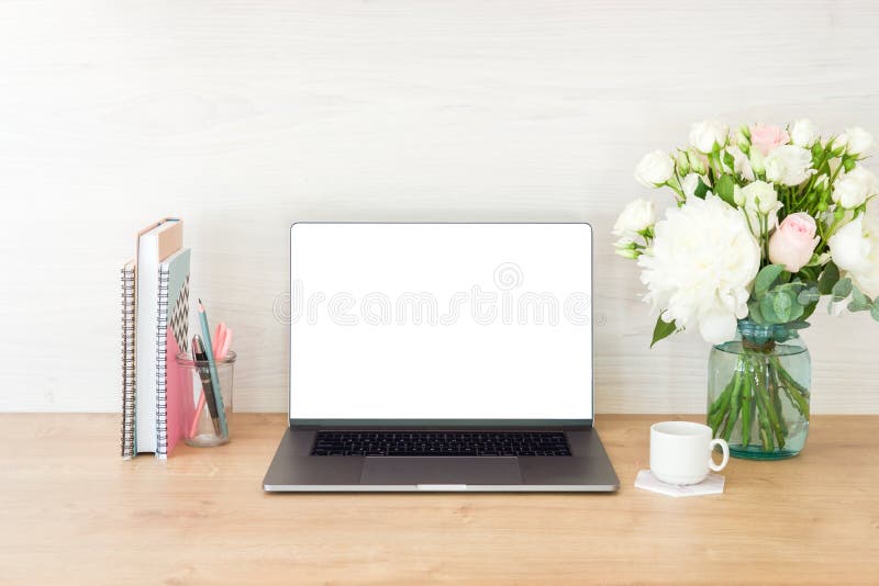 Workspace with laptop computer with blank white screen, feminine office supplies, flowers, books, stationery, coffee cup on wooden royalty free stock photography