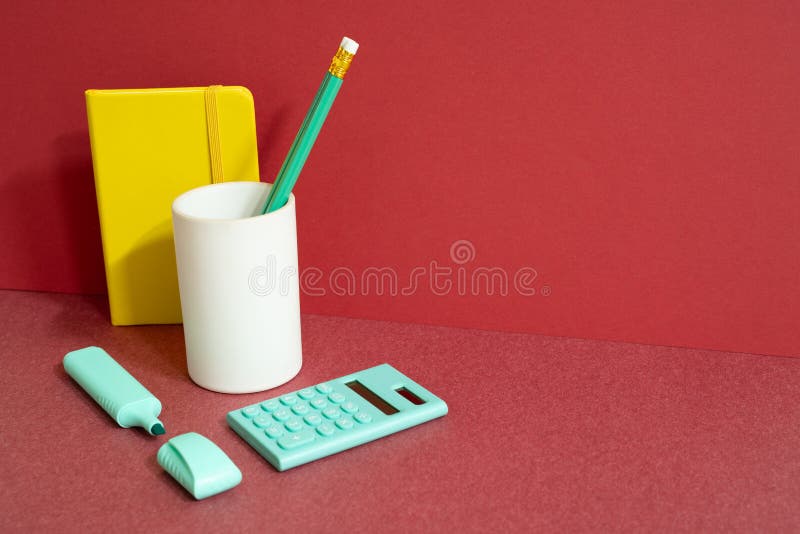 Workspace office supply stationery with note, pencil holder, highlighter calculator on red desk. red wall background. studio shot