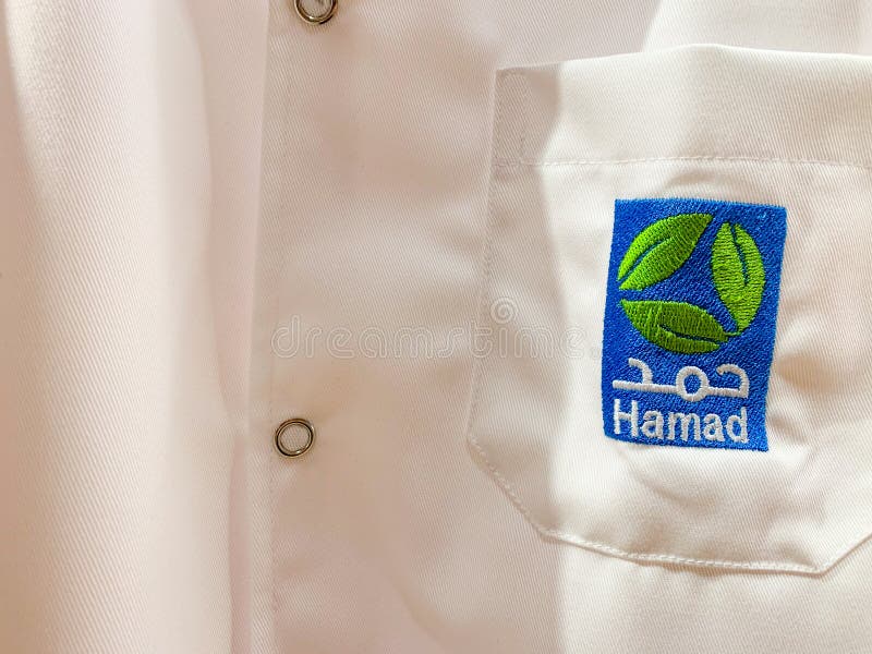 Workwear blanco de un doctor o de un ayudante con el logotipo de Hamad en árabe e inglés Hamad HMC es el proveedor médico más gra foto de archivo libre de regalías Workwear blanco de un doctor o de un ayudante con el logotipo de Hamad en árabe e inglés Hamad HMC es el proveedor médico más gra foto de archivo libre de regalías