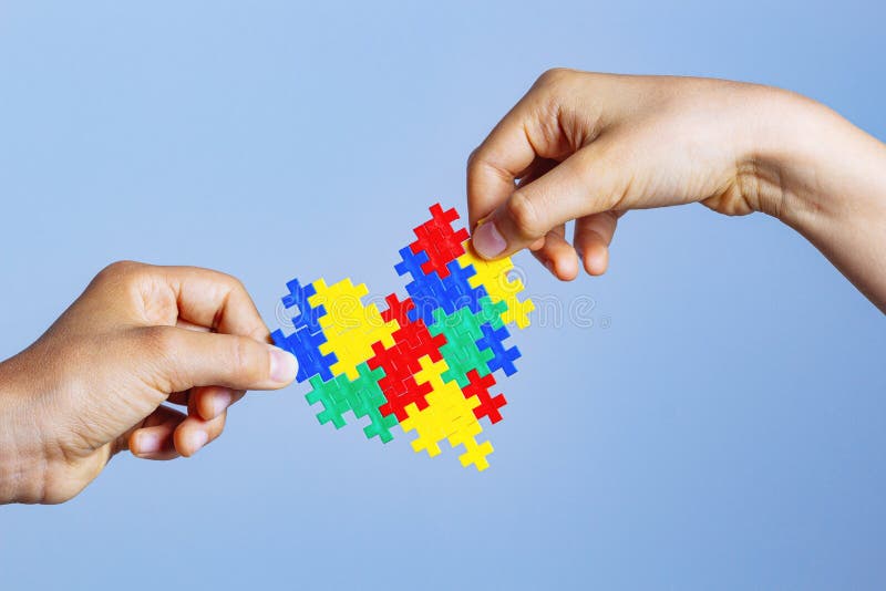 World autism awareness day concept. Children hands holding colorful puzzle heart on blue background