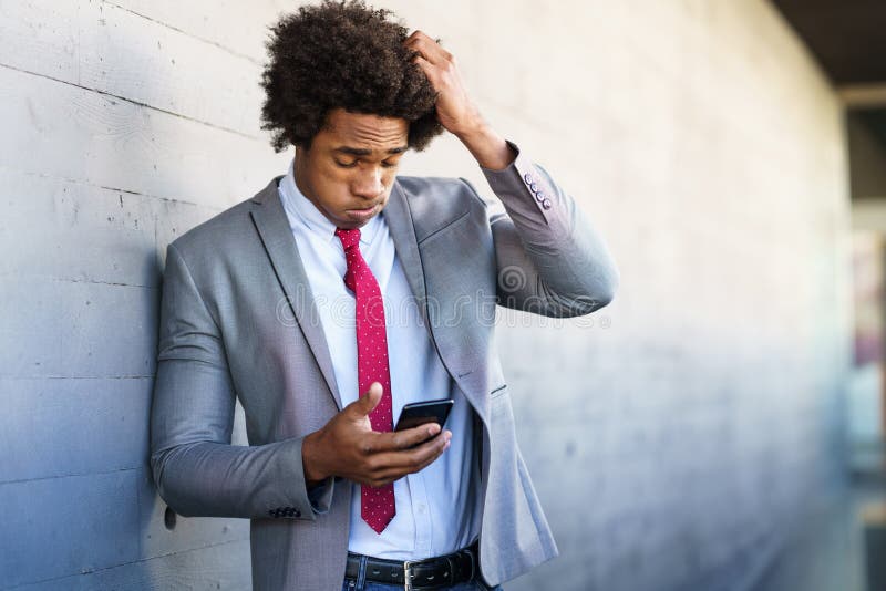 Worried Black Businessman using his smartphone outdoors.