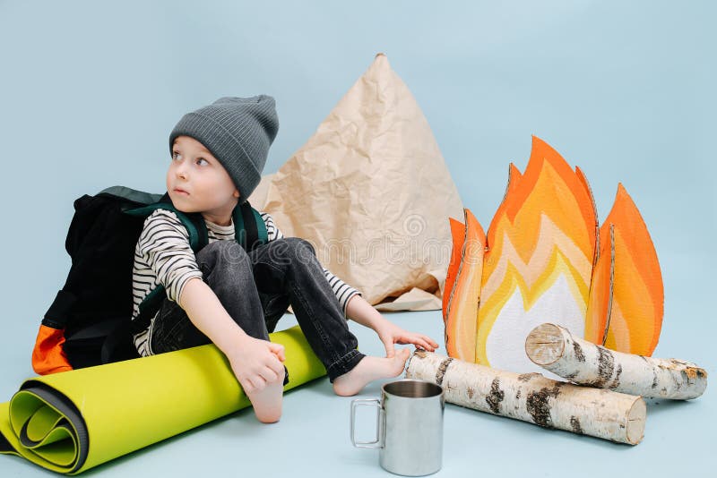 Worried little boy sitting next to a fake campfire, looking over the shoulder