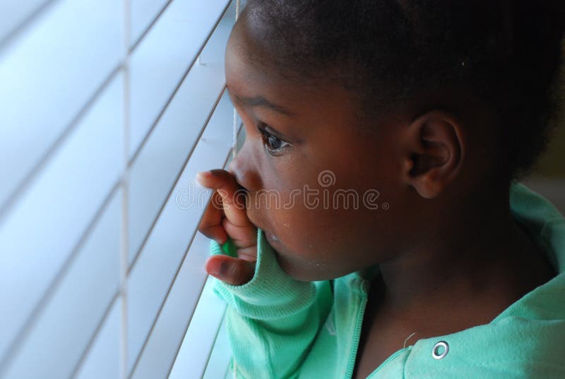 Una bambina che fa capolino attraverso le tende in camera sua per vedere cosa succede fuori.