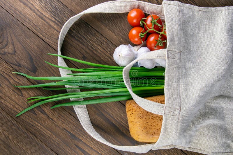 Woven bag of different health food on dark wooden table background. Bread, green onion, garlic, tomato and yellow peper. Top view stock photo