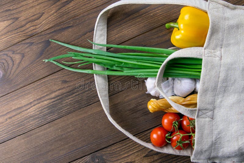 Woven bag of different health food on dark wooden table background. Green onion, garlic, tomato and yellow peper. Top view with royalty free stock images