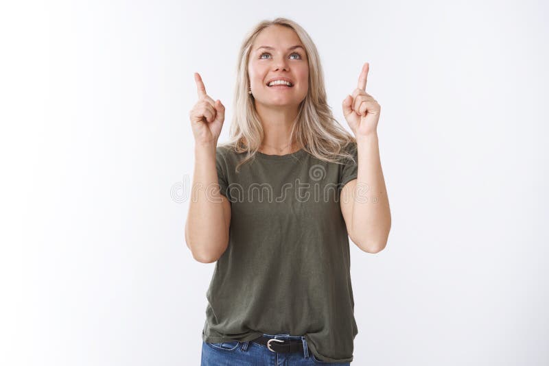 Wow how amusing. Portrait of fascinated amazed and joyful young beautiful woman with blond hair looking pointing up smiling from thrill and joy loving gazing sky over white background.