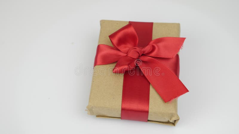 Wrapped gift box with red ribbon tied bow is rotating against white background. Valentine`s Day holiday present surprise. Gift wit