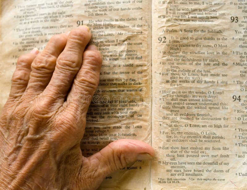 Wrinkled, arthritic left hand on a wrinkled, yellow, worn out, bible turned to Psalm 91.