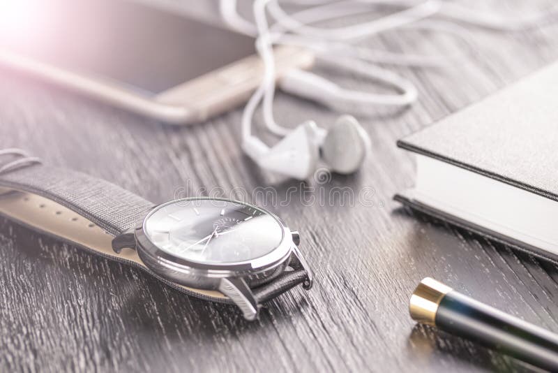 Wristwatch, κινητό τηλέφωνο με τα ακουστικά και ένα σημειωματάριο με μια μάνδρα σε έναν παλαιό σκοτεινό υπολογιστή γραφείου γραφε στοκ φωτογραφία Wristwatch, κινητό τηλέφωνο με τα ακουστικά και ένα σημειωματάριο με μια μάνδρα σε έναν παλαιό σκοτεινό υπολογιστή γραφείου γραφε στοκ φωτογραφία