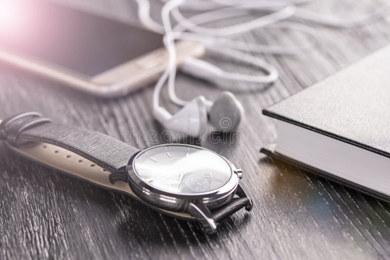 Wristwatch, κινητό τηλέφωνο με τα ακουστικά και σημειωματάριο σε έναν παλαιό σκοτεινό υπολογιστή γραφείου γραφείων στοκ φωτογραφία με δικαίωμα ελεύθερης χρήσης Wristwatch, κινητό τηλέφωνο με τα ακουστικά και σημειωματάριο σε έναν παλαιό σκοτεινό υπολογιστή γραφείου γραφείων στοκ φωτογραφία με δικαίωμα ελεύθερης χρήσης