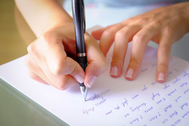 Girl Writing down a letter on a white sheet of paper with a black pen.