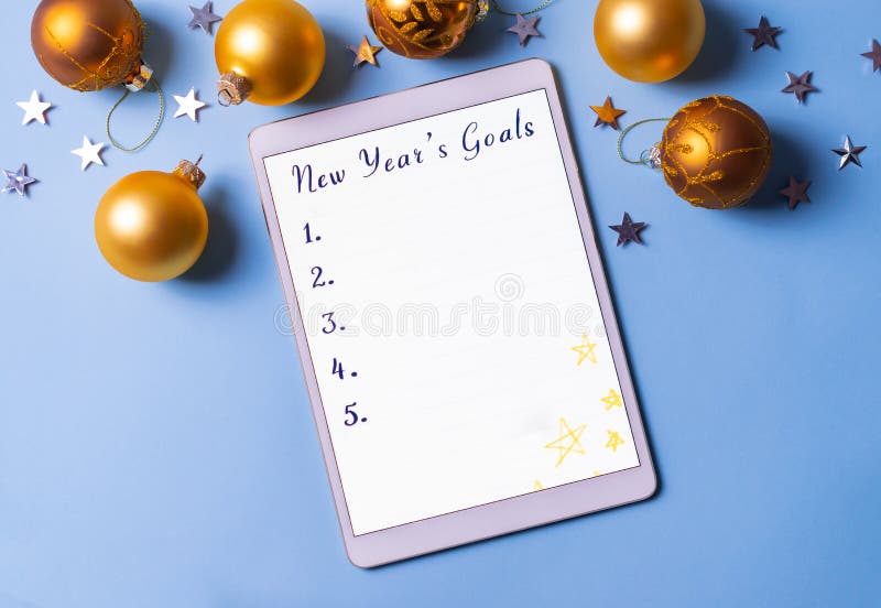 Writing new year`s resolutions and goals list on a tablet on blue background with christmas golden balls