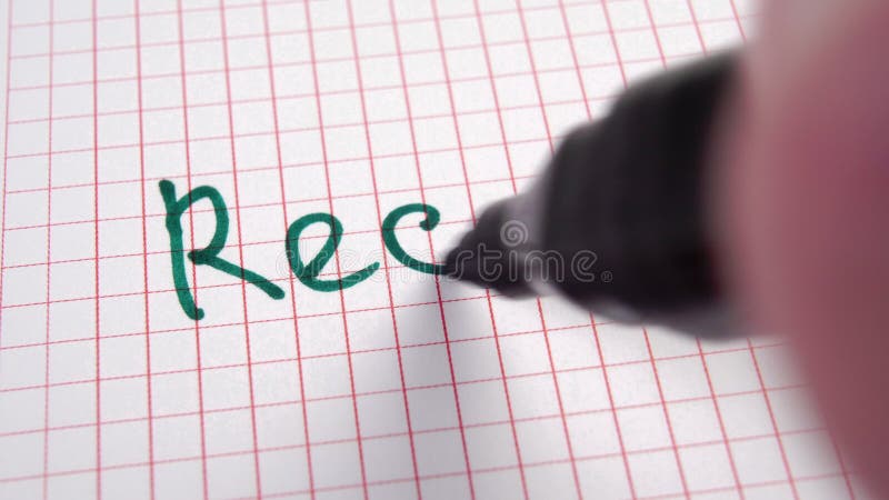 Writing the word RECYCLE in a green felt-tip pen on a squared page of a paper notepad.