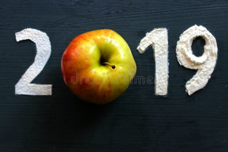 2019 written in flour on a black wooden background, ripe Apple as a symbol of healthy eating