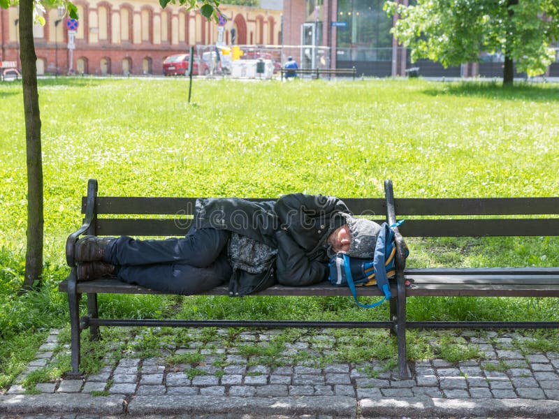 WrocÅ‚aw, Poland - May 24 2019: Homeless man is sleeping on a bench near a newly built stock photos WrocÅ‚aw, Poland - May 24 2019: Homeless man is sleeping on a bench near a newly built stock photos