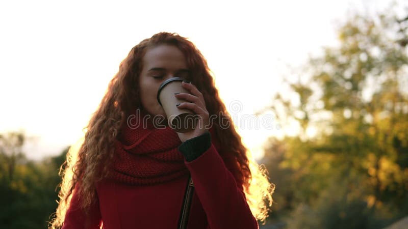 Wspaniała błogości scena dziewczyna stoi outdoors w enjoyng i parku jej kawa Piękna młoda kobieta z długą czerwienią