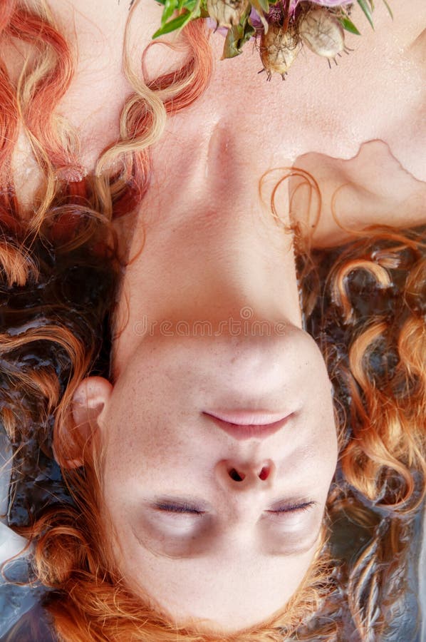 Wspaniały portret młoda kobieta Ophelia z kędzierzawym czerwonym włosianym lying on the beach z kwiatami z oczami zamykał konanie obraz stock Wspaniały portret młoda kobieta Ophelia z kędzierzawym czerwonym włosianym lying on the beach z kwiatami z oczami zamykał konanie obraz stock