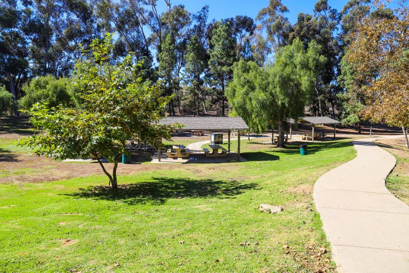 A gorgeous shot of an autumn day in the park with lush green grass, green and autumn colored trees, brown wooden pergolas, a smooth footpath and blue sky at Kenneth Hahn Recreation Area in Los Angeles California USA. A gorgeous shot of an autumn day in the park with lush green grass, green and autumn colored trees, brown wooden pergolas, a smooth footpath and blue sky at Kenneth Hahn Recreation Area in Los Angeles California USA