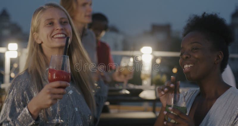 Wunderschöne junge Freundinnen, die Cocktailbrillen beim Tanzen und Sprechen bei Schülerfeiern abends vorstellen