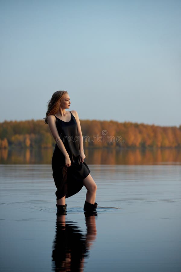 Wunderschöne sexy Frau steht im Wasser durch den Teich in den Sonnenstrahlen untergehenden Sonne stockfoto