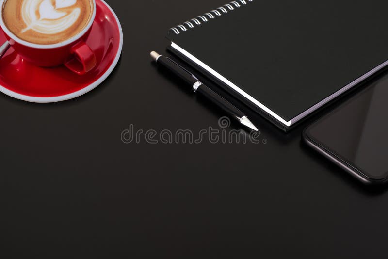 Wybrany czarny, spiralny notebook czarny pióro, smartfon i czerwona filiżanka kawy na czarnym biurku obraz royalty free Wybrany czarny, spiralny notebook czarny pióro, smartfon i czerwona filiżanka kawy na czarnym biurku obraz royalty free