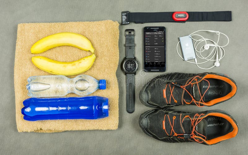 Niedomice, Poland - June 08, 2018: Equipment for a runner training. Pulse measurement kit - a heart rate monitor Garmin, an isotonic drink, bananas, a towel, an iPod with dry jackets Apple and running shoes Dynafit. Niedomice, Poland - June 08, 2018: Equipment for a runner training. Pulse measurement kit - a heart rate monitor Garmin, an isotonic drink, bananas, a towel, an iPod with dry jackets Apple and running shoes Dynafit.