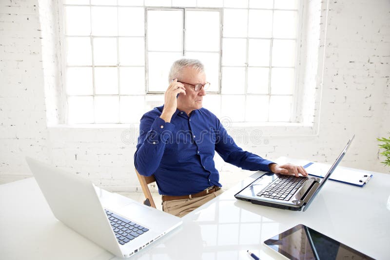 Wysoki kąt strzelał starszy biznesmen opowiada z somebody na jego telefonie komórkowym podczas gdy pracujący na laptopach obrazy stock Wysoki kąt strzelał starszy biznesmen opowiada z somebody na jego telefonie komórkowym podczas gdy pracujący na laptopach obrazy stock