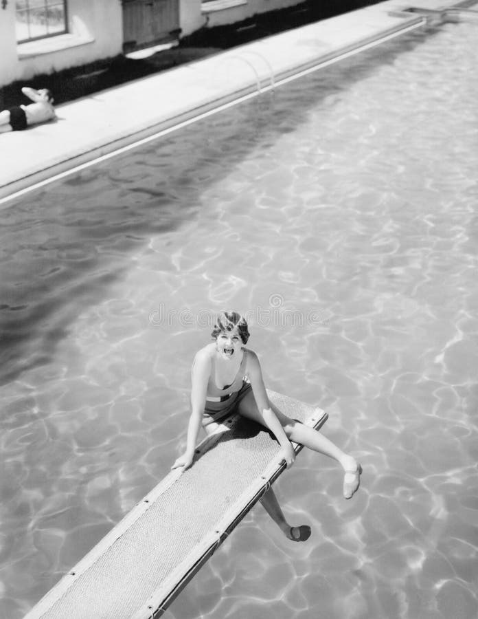 High angle view of a woman sitting on a diving board and looking feared (All persons depicted are no longer living and no estate exists. Supplier grants that there will be no model release issues.). High angle view of a woman sitting on a diving board and looking feared (All persons depicted are no longer living and no estate exists. Supplier grants that there will be no model release issues.)