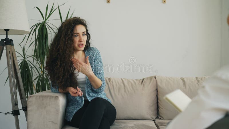 Wzburzona młoda kobieta opowiada o jej problemach z fachowym żeńskim psychoanalitykiem w psychoterapeuta biurze indoors zdjęcie wideo Wzburzona młoda kobieta opowiada o jej problemach z fachowym żeńskim psychoanalitykiem w psychoterapeuta biurze indoors zdjęcie wideo