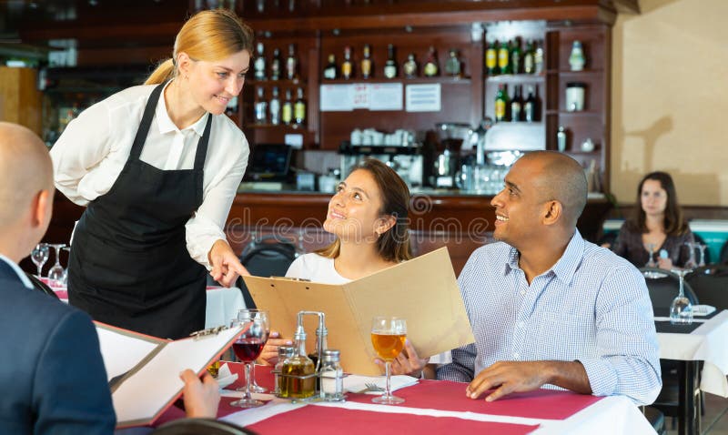 Restaurant guests will choose dish from the menu. Polite waitress helps with the choice. Restaurant guests will choose dish from the menu. Polite waitress helps with the choice