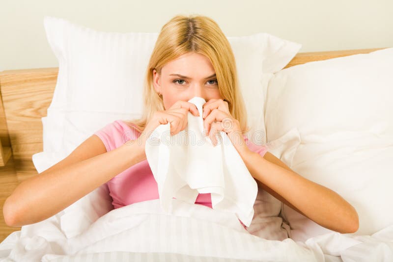 Photo of sick woman sitting in bed with tissue and blowing her nose into it. Photo of sick woman sitting in bed with tissue and blowing her nose into it