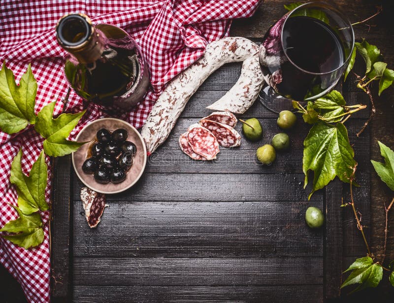 Włoski jedzenia wciąż życie z butelką i szkłem czerwone wino, oliwki i kiełbasa na ciemnym nieociosanym tle, odgórny widok fotografia stock Włoski jedzenia wciąż życie z butelką i szkłem czerwone wino, oliwki i kiełbasa na ciemnym nieociosanym tle, odgórny widok fotografia stock