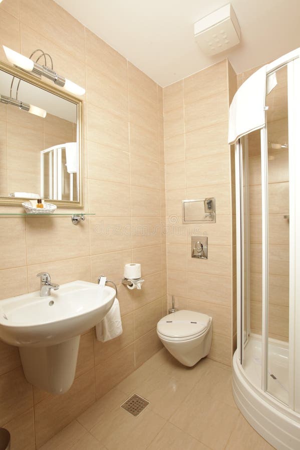 Picture of a clean luxury bathroom includes a shower cabin, mirror, sink and toilet. Walls and floor are covered with brown marble. Picture of a clean luxury bathroom includes a shower cabin, mirror, sink and toilet. Walls and floor are covered with brown marble.