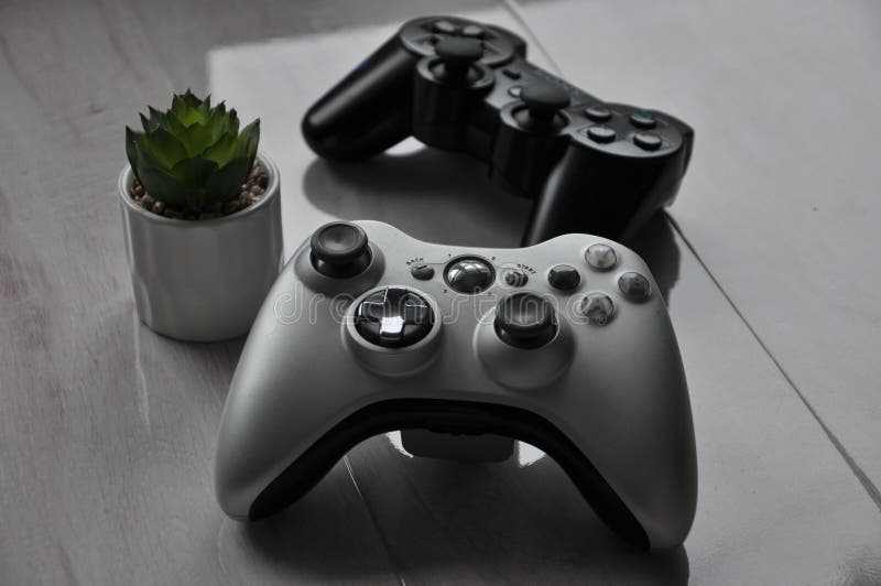 Gray Xbox 360 controller in front with black Playstation 3 controller in background. Gray Xbox 360 controller in front with black Playstation 3 controller in background