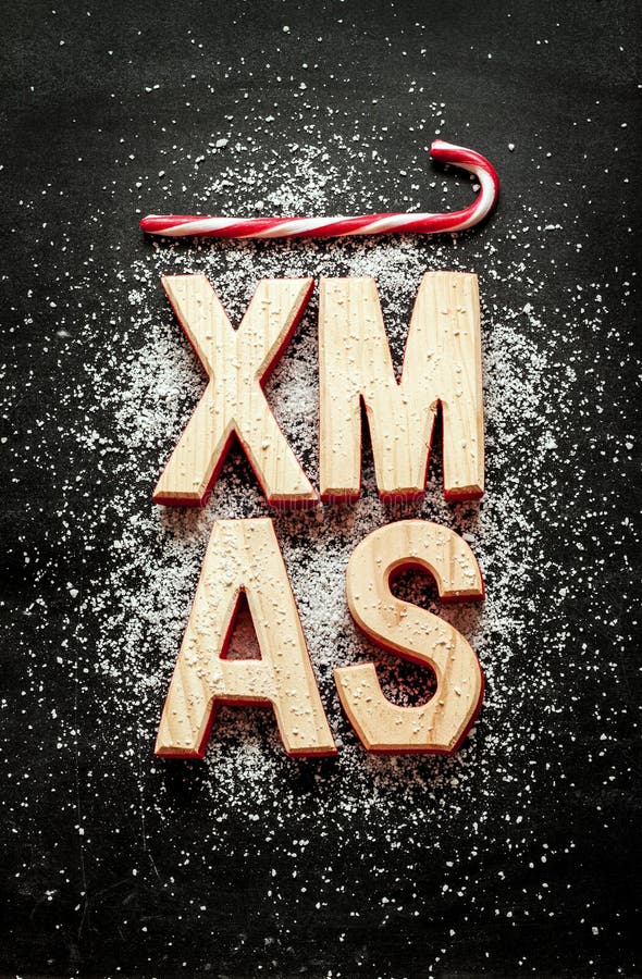 'Xmas' wooden letters, sugar as snow and red candy canes on black chalkboard background. Christmas poster concept captured from above - vintage mood.