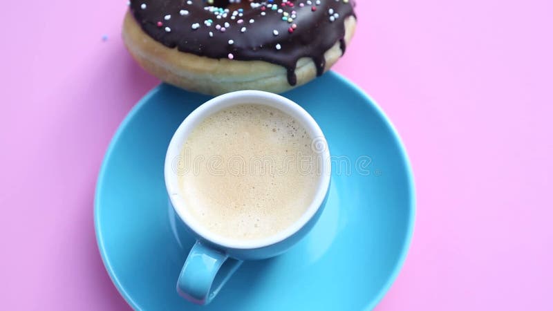 Xícara de café azul com a filhós do chocolate em girar a placa cor-de-rosa