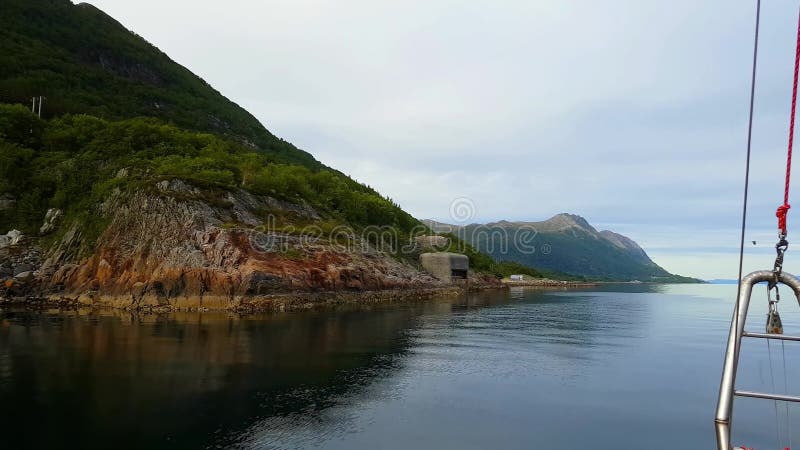 Yachtsegling längs grön bergig kust i stillhetvatten någonstans i Norge