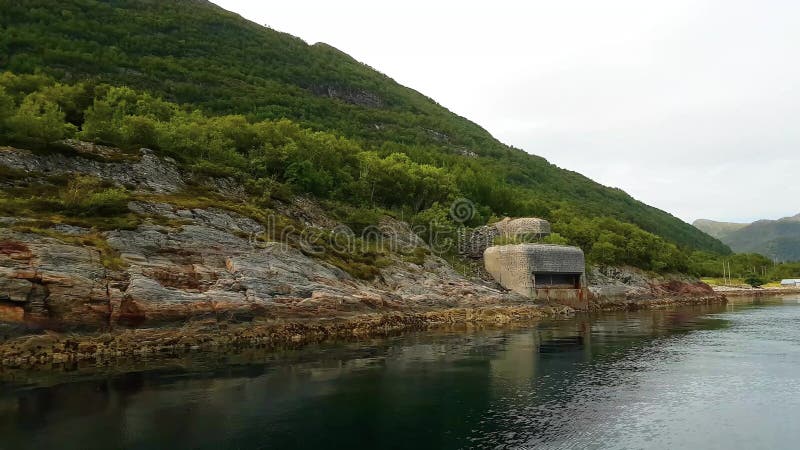 Yachtsegling längs grön bergig kust med pillerasken av det andra världskriget i stillhetvatten någonstans i Norge