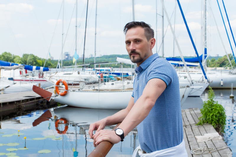 Yachtsman standing near of pier barrier with boats. Bearded man looking to far before journey near of yacht. royalty free stock photography Yachtsman standing near of pier barrier with boats. Bearded man looking to far before journey near of yacht. royalty free stock photography