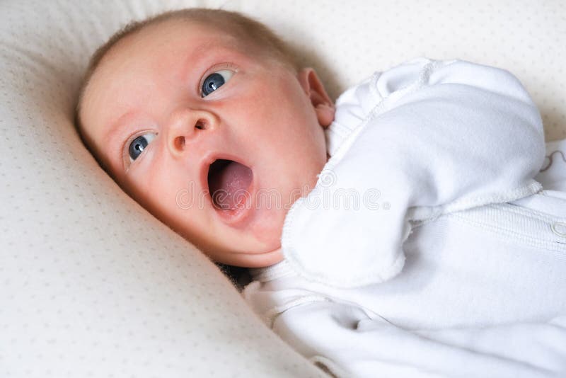 Yawning cute newborn baby boy lying in bed trying to sleep. Baby sleeplessness. stock photography