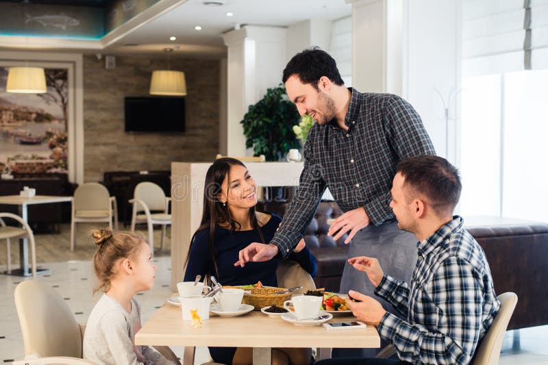 Życzliwy uśmiechnięty kelner bierze rozkaz przy stołem rodzinny wpólnie mieć gościa restauracji zdjęcia stock Życzliwy uśmiechnięty kelner bierze rozkaz przy stołem rodzinny wpólnie mieć gościa restauracji zdjęcia stock