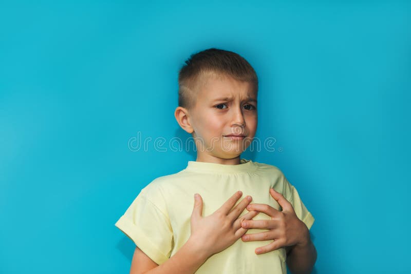 A 6-7 year old boy in a yellow T-shirt shows a gesture of being bored, upset on a blue background, front view