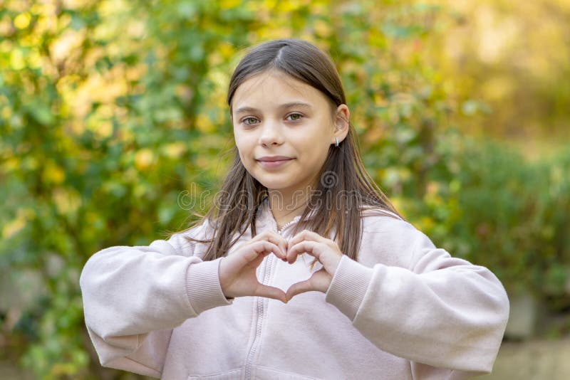 A 10-12-year-old Girl in Pink Pajamas Shows a Heart Sign with Her Hands  Against the Background of Nature. Stock Photo - Image of girl, person:  260526280