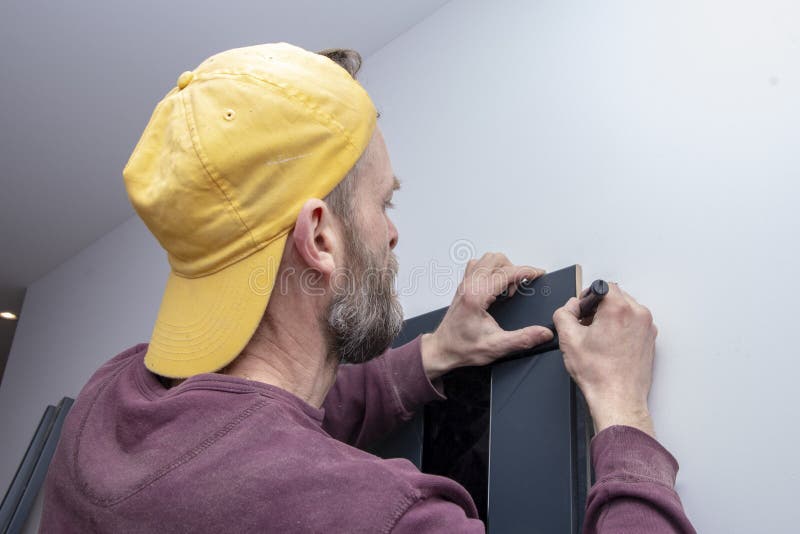 45-50-year-old male construction worker MARKS out the trim on the wooden doors with a PENCIL; Concept: interior decoration