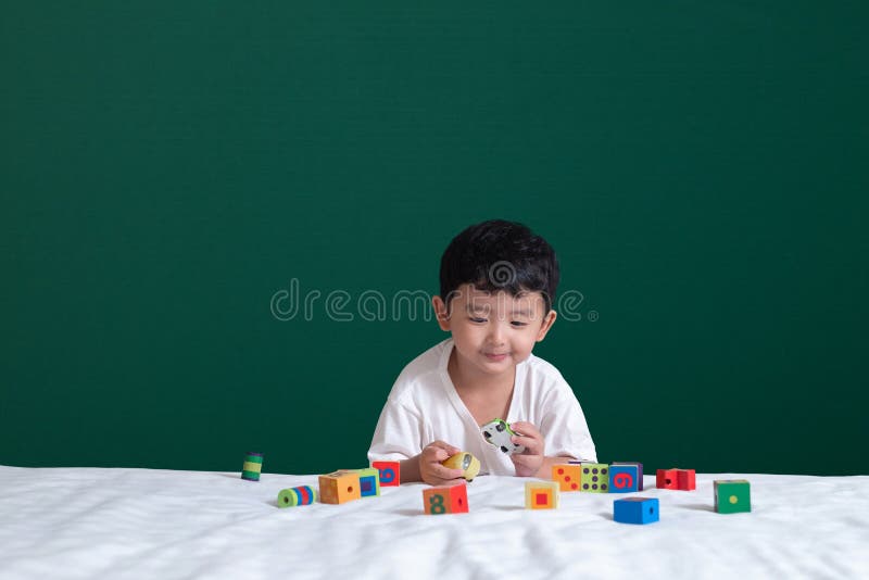 3 years old Asian boy play toy or square block puzzle on green chalkboard or school board background, kid lying learn by playing