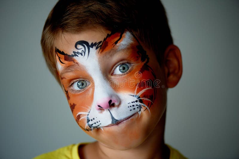 Years old boy with blue eyes face painting of a cat or tiger. Orange.