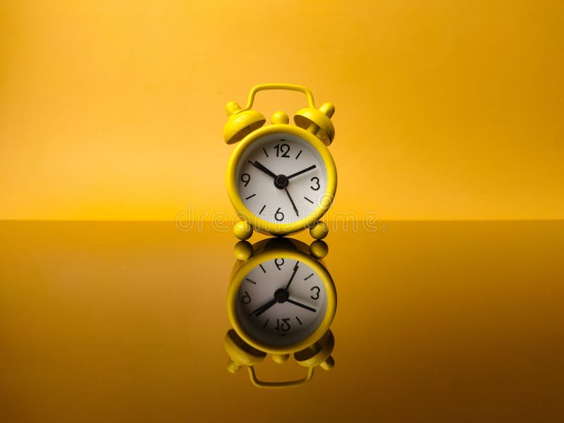 Yellow alarm clock on yellow background with reflection stock photography