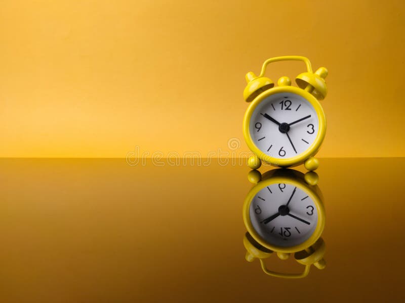 Yellow alarm clock on yellow background with reflection on a black acrylic board stock photo