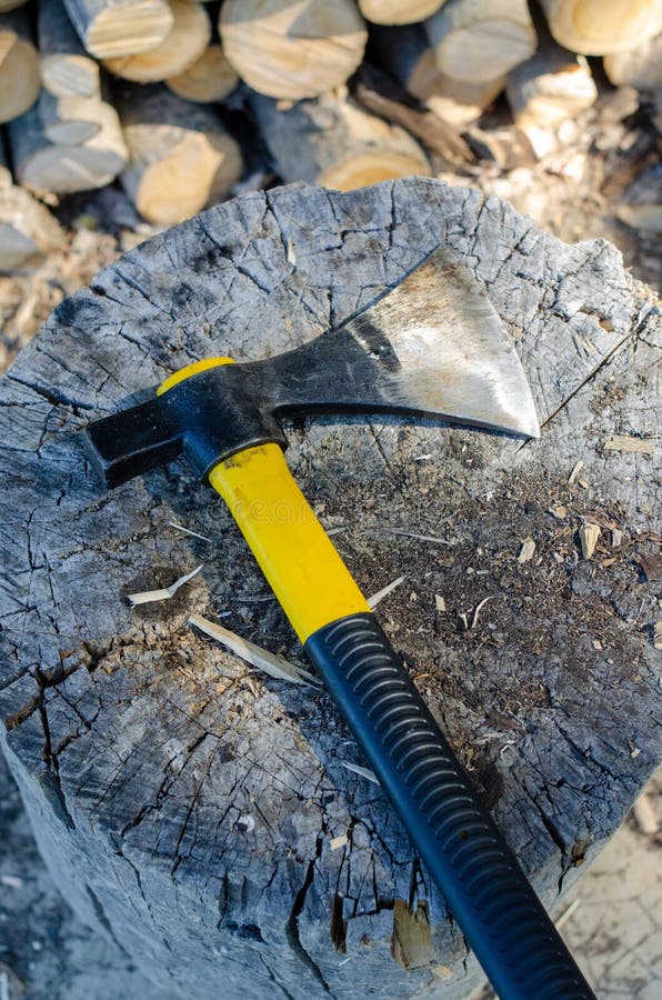 Axe with a piece of wood near a stack of logs stock images