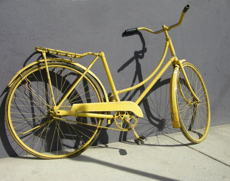 An old yellow bike leaning on a grey wall